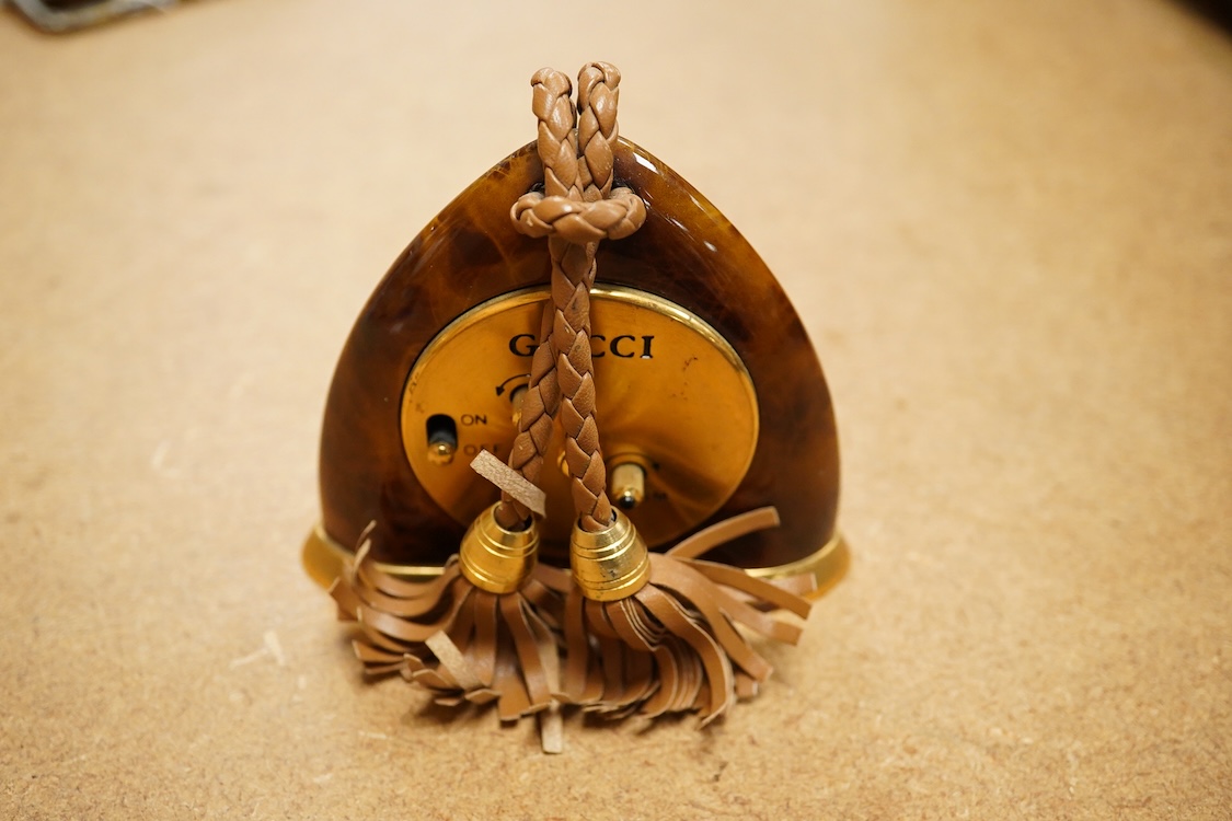 A Gucci gilt and enamelled stirrup shaped alarm clock with plaited and tasselled leather decoration, 9cm high